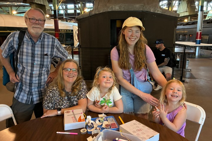 Smiling group of adults and children at a table with crafts in a train station.