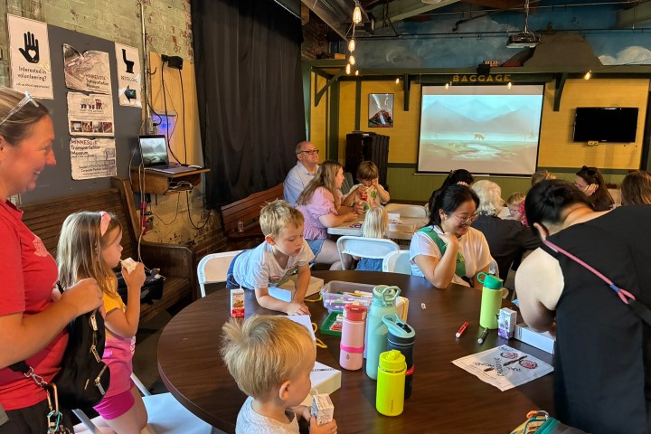 Children and adults sitting at tables in a rustic room, engaged in activities.
