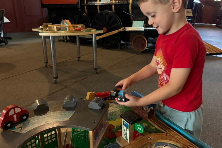 Young boy playing with toy trains on a table in a museum setting.