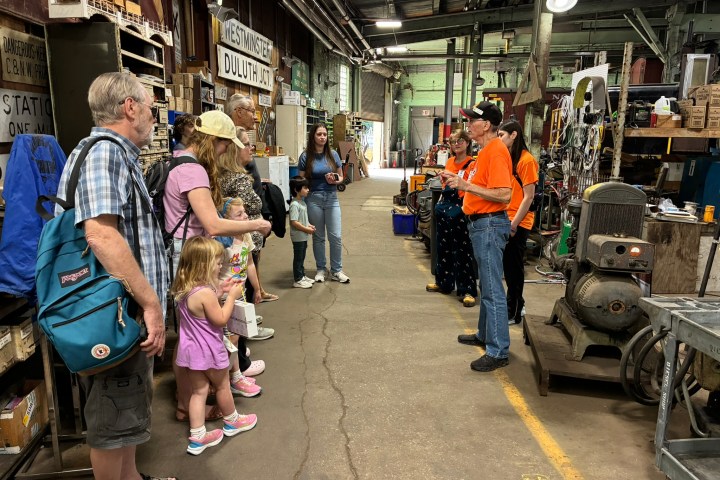 A tour group listens to a guide in a cluttered industrial workshop.