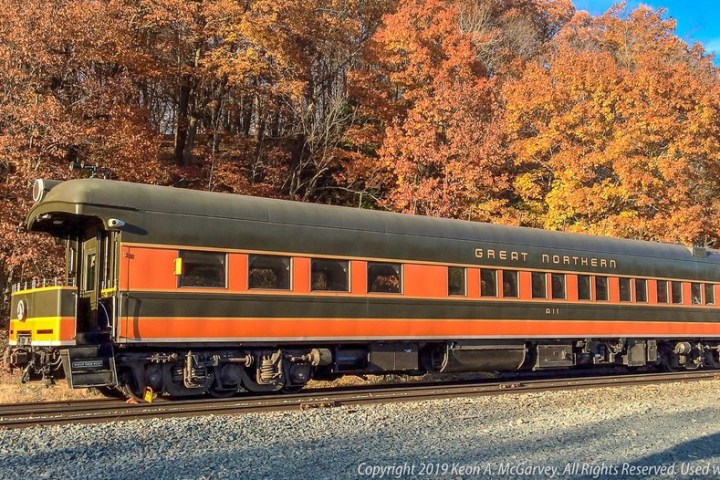 an orange train traveling down train tracks near a forest