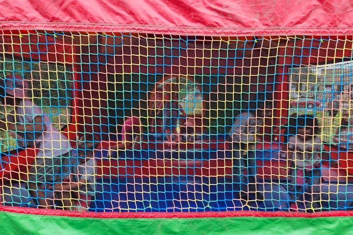 Children playing inside a colorful inflatable bounce house with netting.