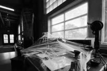 Desk covered in cobwebs in a dimly lit room with large windows and microphone.