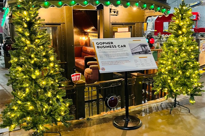 Vintage train car with lights and two decorated trees inside an industrial venue.