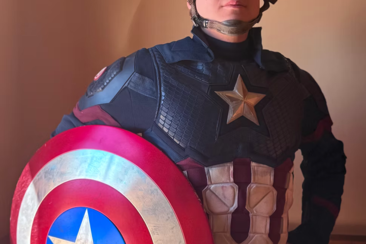 Person in Captain America costume with shield poses indoors.