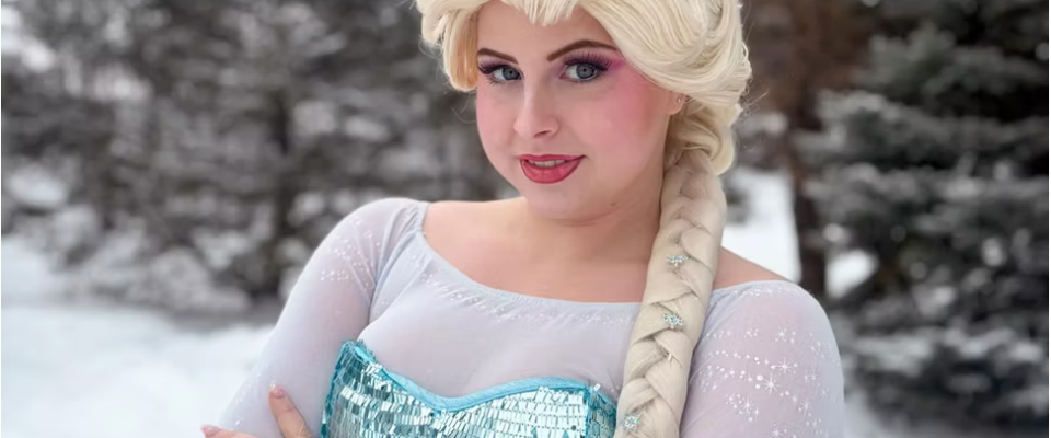 Person in a light blue dress with braided blonde hair, standing in snowy landscape.