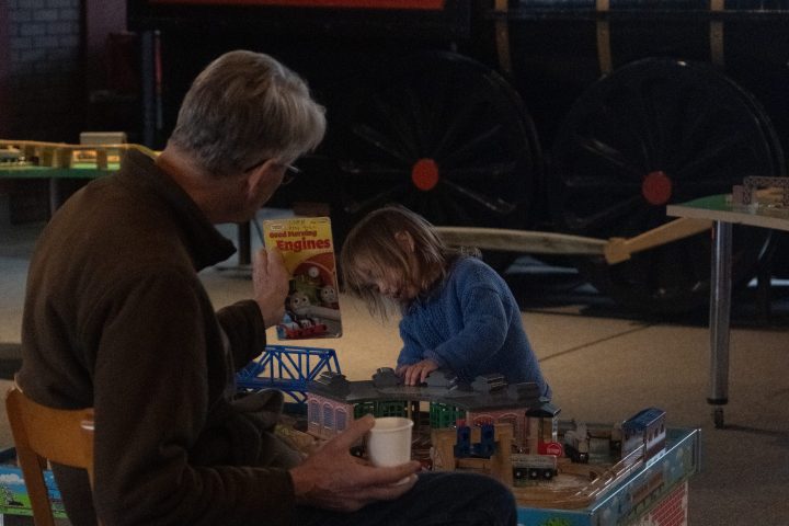 Man and child playing with a train set in dim lighting.